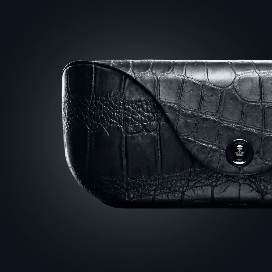 Close-up of a Ray-Ban case: black alligator leather, a flap, and a snap button crowned with the Caviar emblem